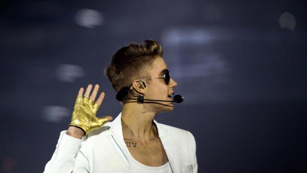 Justin Bieber tritt mit Sonnenbrille und goldenem Handschuh auf einer Bühne auf.