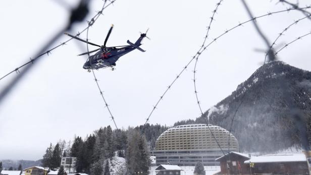 Ein Hubschrauber fliegt vor einer verschneiten Landschaft mit einem markanten Gebäude und einem Berg im Hintergrund.