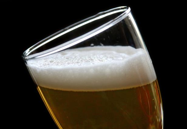 Ein Glas helles Bier mit Schaum vor einem schwarzen Hintergrund.