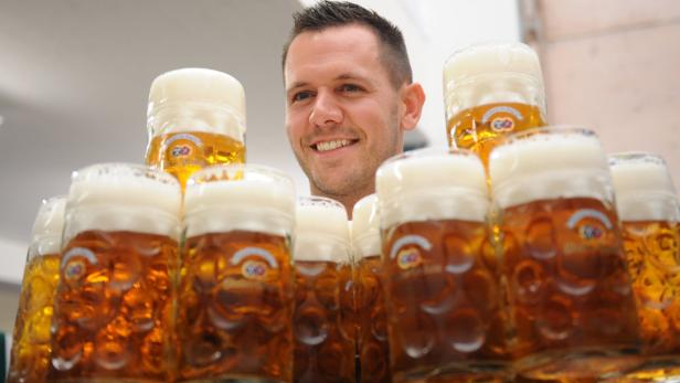 Ein lächelnder Mann steht hinter einem Stapel voller Bierkrüge.