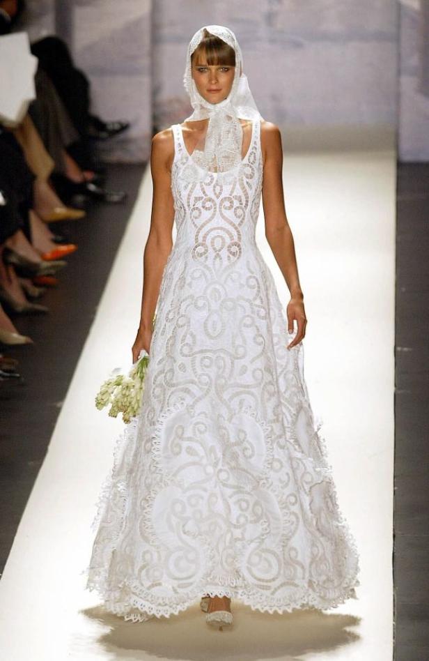 Eine Frau in einem weißen Spitzenkleid und Schleier auf dem Laufsteg.