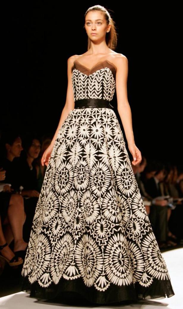 Ein Model präsentiert ein trägerloses, schwarz-weiß gemustertes Kleid mit einem schwarzen Gürtel auf dem Laufsteg.