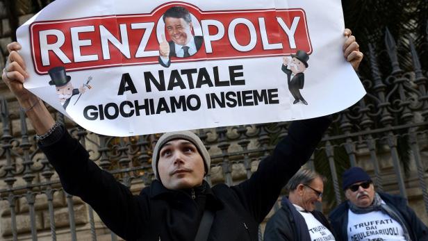 ITALY-ECONOMY-BANK-POLITICS-BANKING-DEMO Ein Mann hält ein Schild mit der Aufschrift „RENZOPOLY A NATALE GIOCHIAMO INSIEME“ hoch.