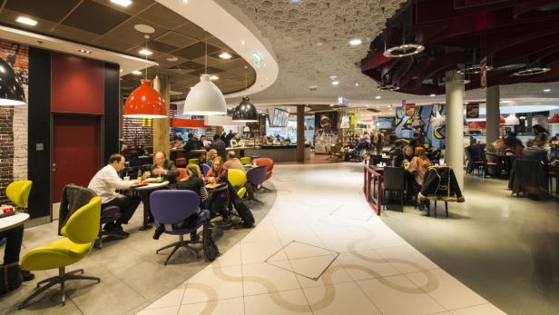 In einem hellen Einkaufszentrum sitzen Menschen an Tischen und essen.