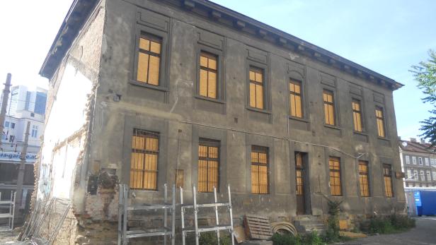 Ein baufälliges, graues Gebäude mit vernagelten Fenstern steht in einer Stadt.