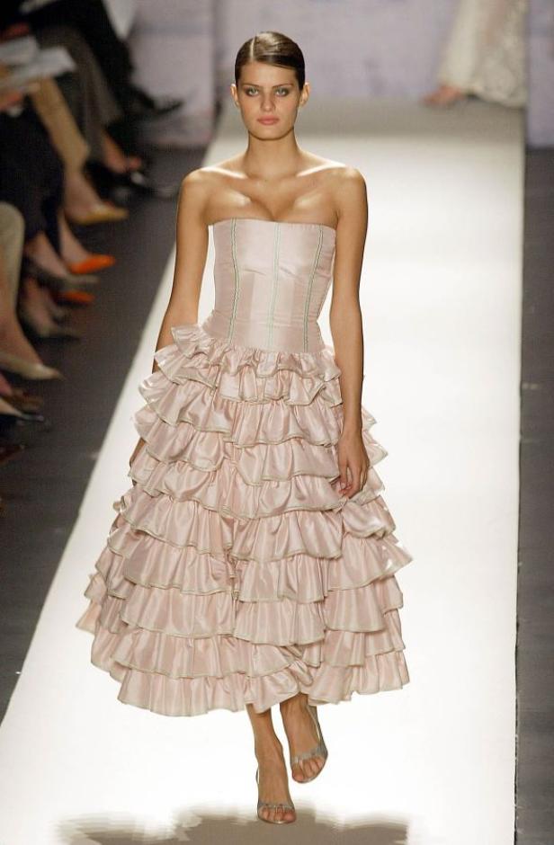 Eine Frau auf dem Laufsteg präsentiert ein trägerloses, rosa Kleid mit Rüschen.