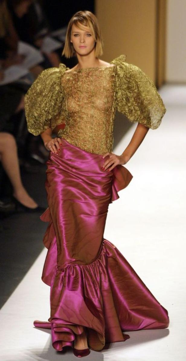Eine Frau präsentiert ein goldenes Oberteil mit Puffärmeln und einen langen, pinkfarbenen Rock auf einem Laufsteg.