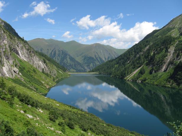Ein Bergsee spiegelt den blauen Himmel und die grünen Hänge wider.