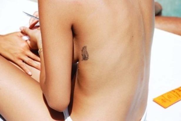 Eine Frau mit einem Feder-Tattoo auf der Rippe sitzt auf einer Liege.