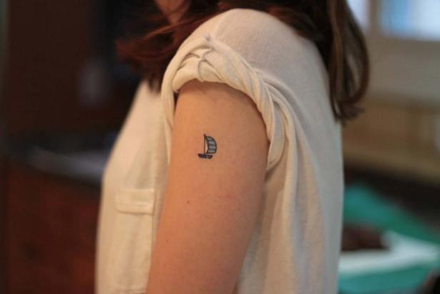 Eine Frau hat ein kleines Segelboot-Tattoo auf ihrem Oberarm.