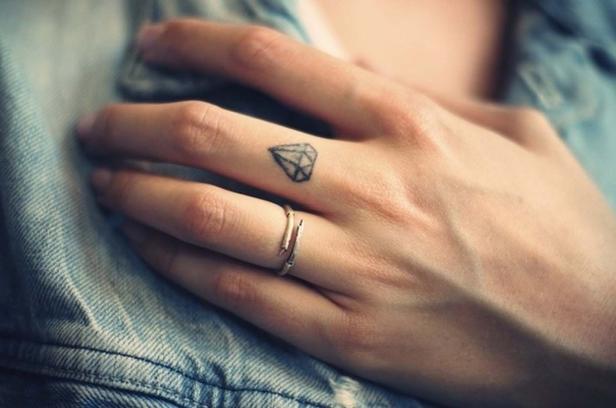 Eine Hand mit einem Diamant-Tattoo auf dem Finger und einem Ring.