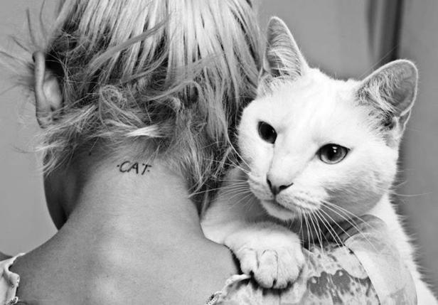 Eine Frau mit einem „Cat“-Tattoo im Nacken hält eine weiße Katze.