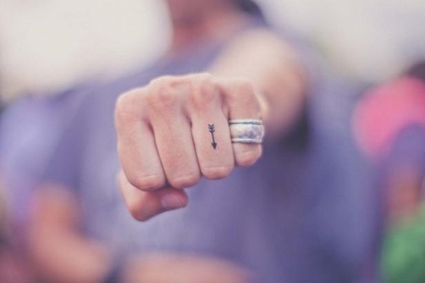 Die Faust einer Person mit einem Pfeil-Tattoo und einem Ring.