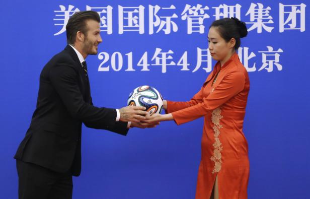 An attendant passes a soccer ball to former captain of England soccer team David Beckham during a ceremony at the Great Hall of the People in Beijing