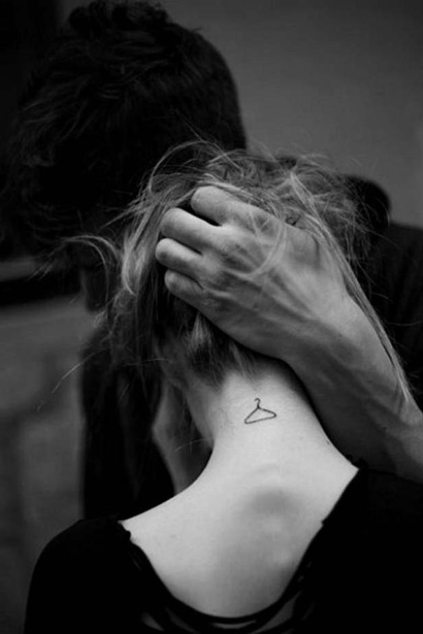 Ein Mann berührt den Nacken einer Frau, die ein Kleiderbügel-Tattoo trägt.