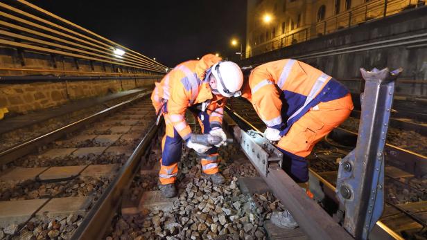 Zwei Bauarbeiter reparieren nachts eine Bahnschiene.