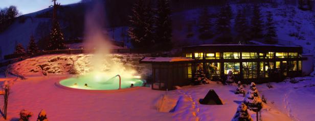 Ein Außenpool mit warmem Wasser und Dampf inmitten einer verschneiten Landschaft bei Nacht.