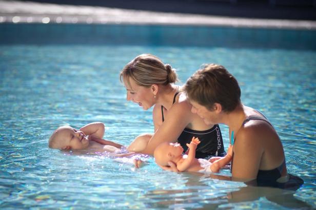 Zwei Frauen und ein Baby schwimmen in einem Schwimmbad, eine Frau hält eine Babypuppe.
