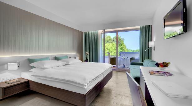 Ein helles Hotelzimmer mit Doppelbett und Balkon mit Blick ins Grüne.