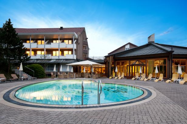 Ein Schwimmbad mit Liegestühlen vor einem Hotelgebäude.