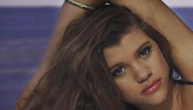 Porträt einer jungen Frau mit braunen Haaren und einem Arm über dem Kopf.