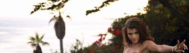 Eine junge Frau posiert vor einer Küstenlandschaft mit Palmen im Hintergrund.