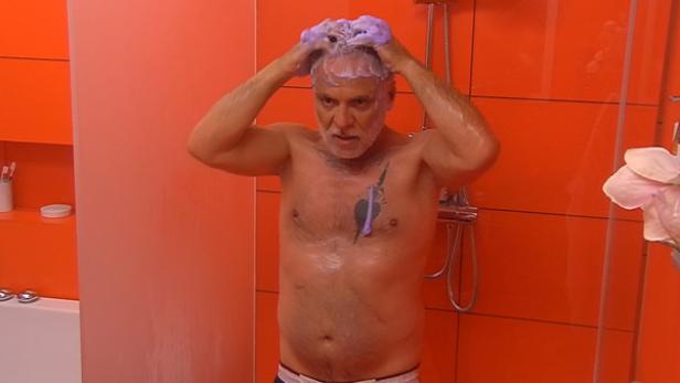 Ein Mann mit Tätowierung wäscht sich die Haare unter der Dusche.