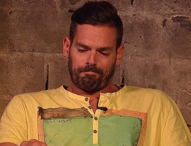 Ein Mann mit Bart und gelbem T-Shirt blickt nach unten.