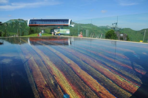 Ein flacher Pool mit einem Holzbodenmuster reflektiert eine Bergbahnstation.