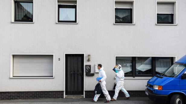 Zwei Personen in Schutzanzügen gehen an einem Haus mit der Nummer 5 vorbei.