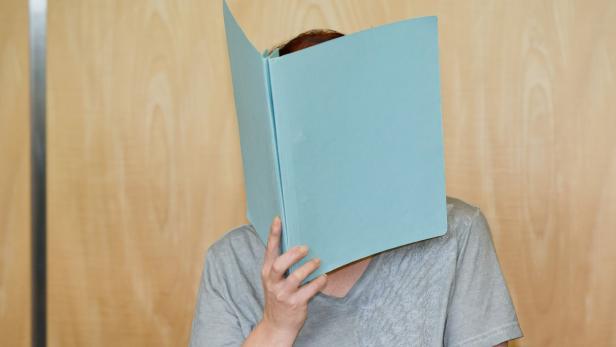 Eine Person hält einen blauen Ordner vor ihr Gesicht.