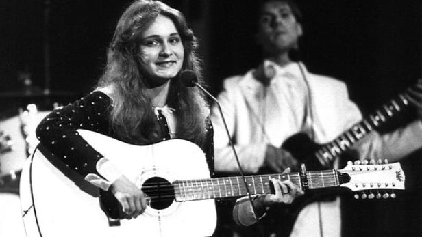 Eine junge Frau spielt auf einer zwölfsaitigen Gitarre und singt in ein Mikrofon.