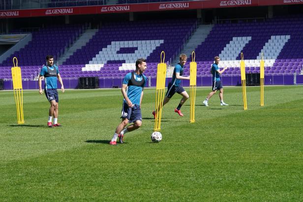 Fußballspieler trainieren mit Dummies auf dem Rasen vor einer Tribüne.