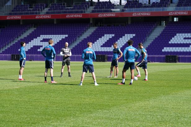 Fußballspieler und ein Trainer stehen auf dem Rasen eines Stadions.