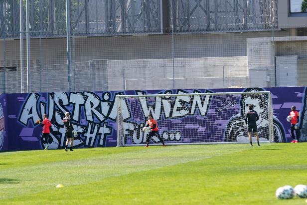 Ein Torwart trainiert vor einer Wand mit Graffiti des Schriftzugs „Austria Wien“.
