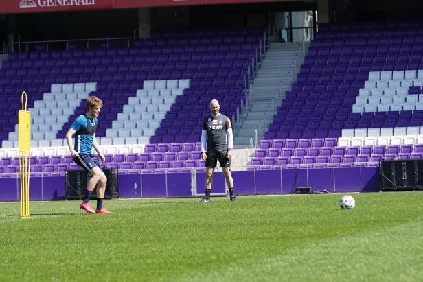 Zwei Fußballspieler trainieren auf dem Rasen vor einer Tribüne.
