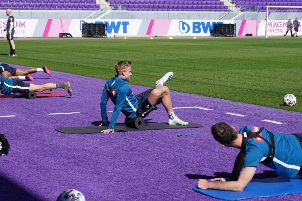 Fußballspieler dehnen sich auf einer lila Trainingsfläche.
