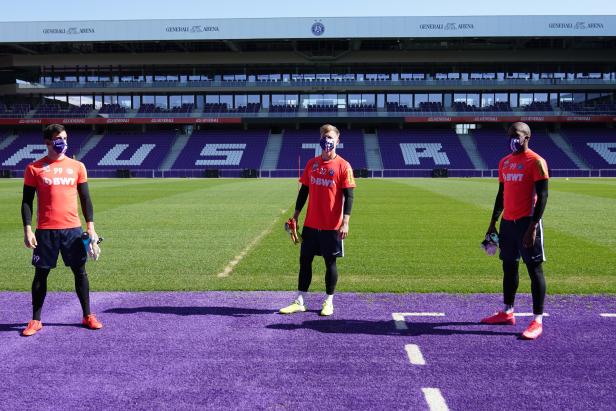Drei Fußballspieler mit Masken stehen im Generali-Arena Stadion.
