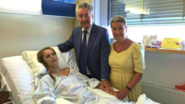 Ein Patientin liegt im Krankenhausbett, besucht von einem älteren Paar.