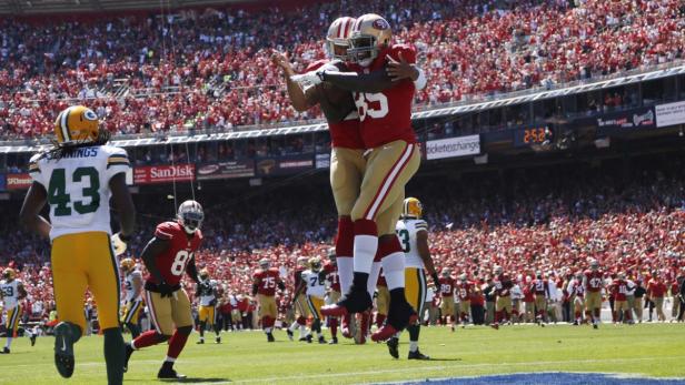 Zwei Footballspieler der San Francisco 49ers feiern einen Touchdown vor einer Zuschauermenge.