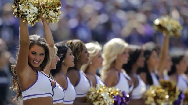 Eine Reihe Cheerleader mit goldenen Pompoms treten bei einem Sportevent auf.