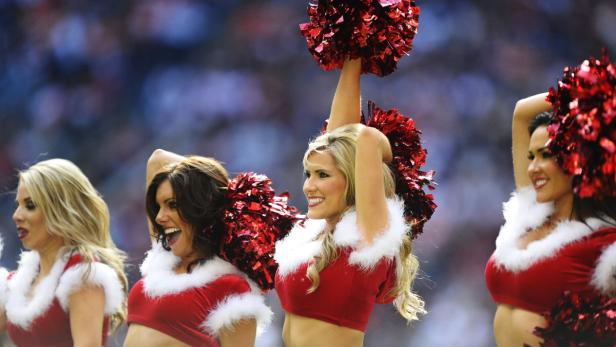 Eine Gruppe Cheerleader in roten Weihnachtskostümen mit Pompoms treten auf.