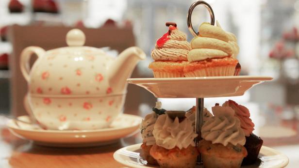 Ein Etageren-Ständer präsentiert eine Auswahl an verzierten Cupcakes neben einer Teekanne.