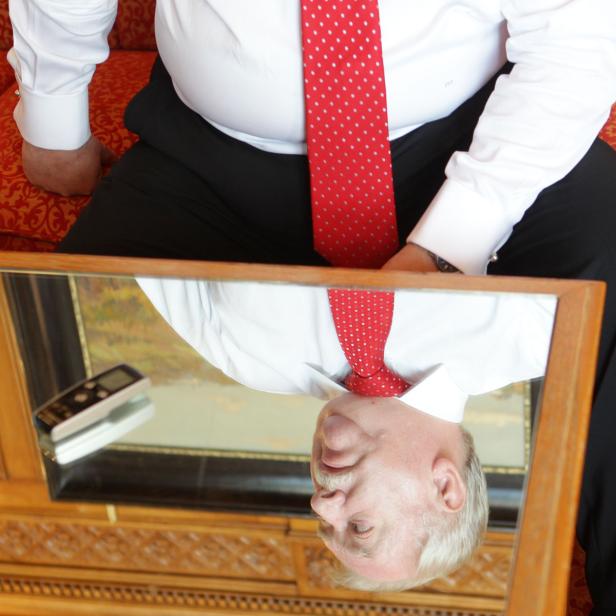 Ein Mann mit roter Krawatte betrachtet sein Spiegelbild.