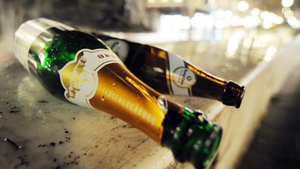 Zwei leere Sektflaschen liegen auf einer Mauer.