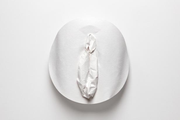 Ein zerknittertes Stück Papier formt eine Vulva auf einem weißen Teller.