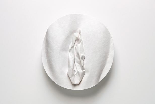 Ein zerknittertes Stück Papier liegt auf einem weißen Teller.