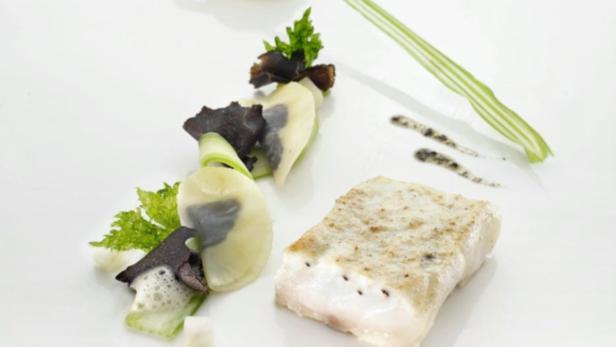 Ein Teller mit einem Stück Fisch, Gemüse und einer dunklen Soße.