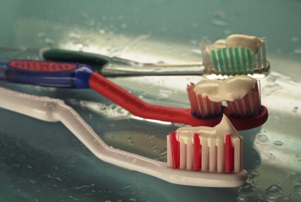 Drei Zahnbürsten mit Zahnpasta liegen auf einer nassen Oberfläche.