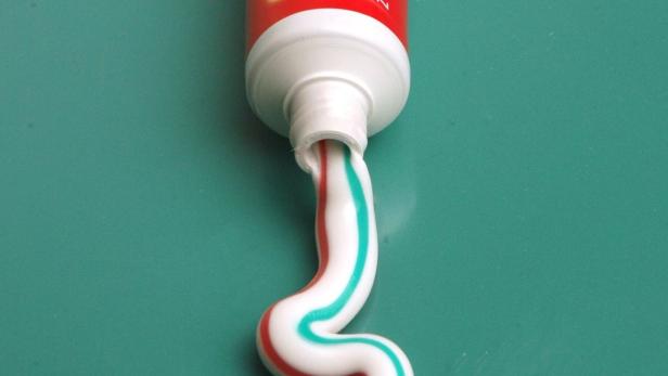 Zahnpasta wird aus einer Tube auf einer türkisfarbenen Oberfläche gedrückt.